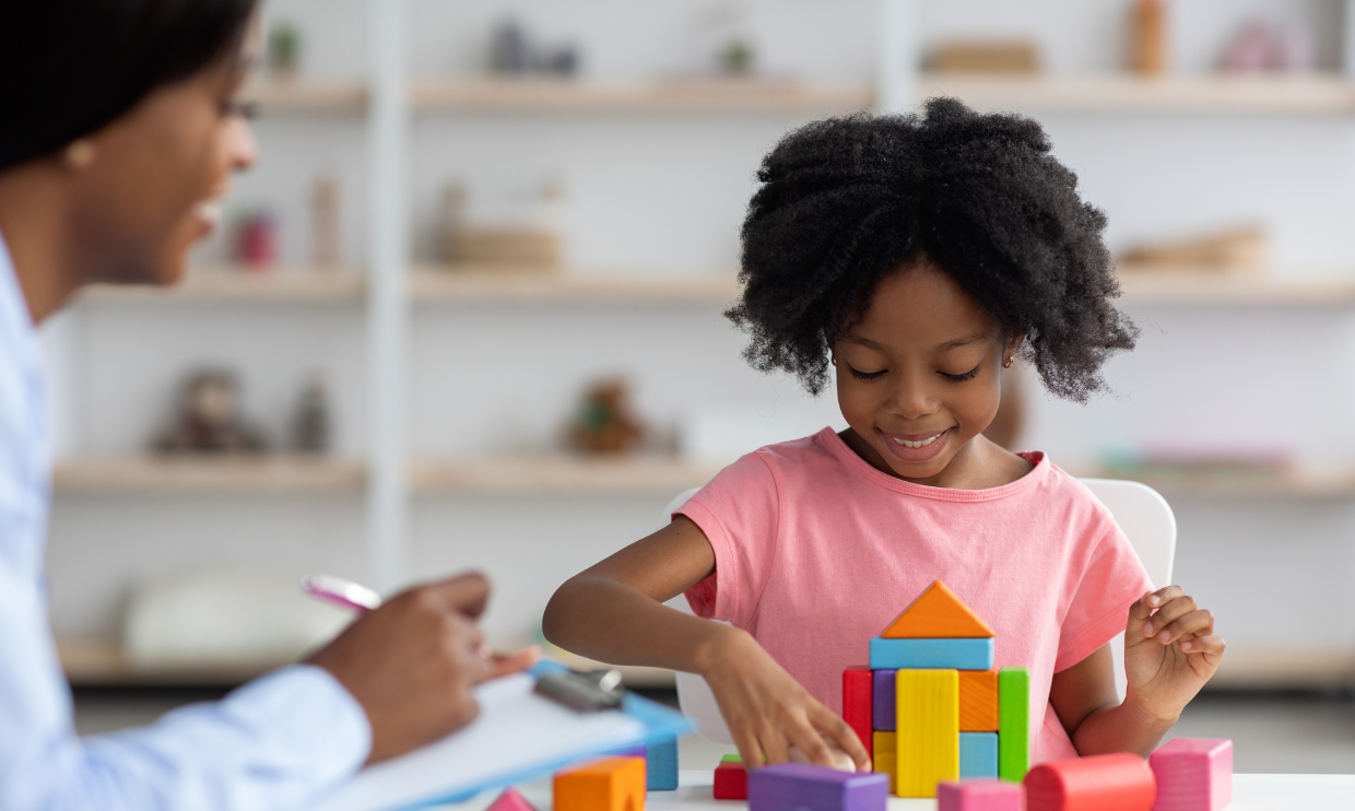 Girl playing blocks while a therapist assesses.